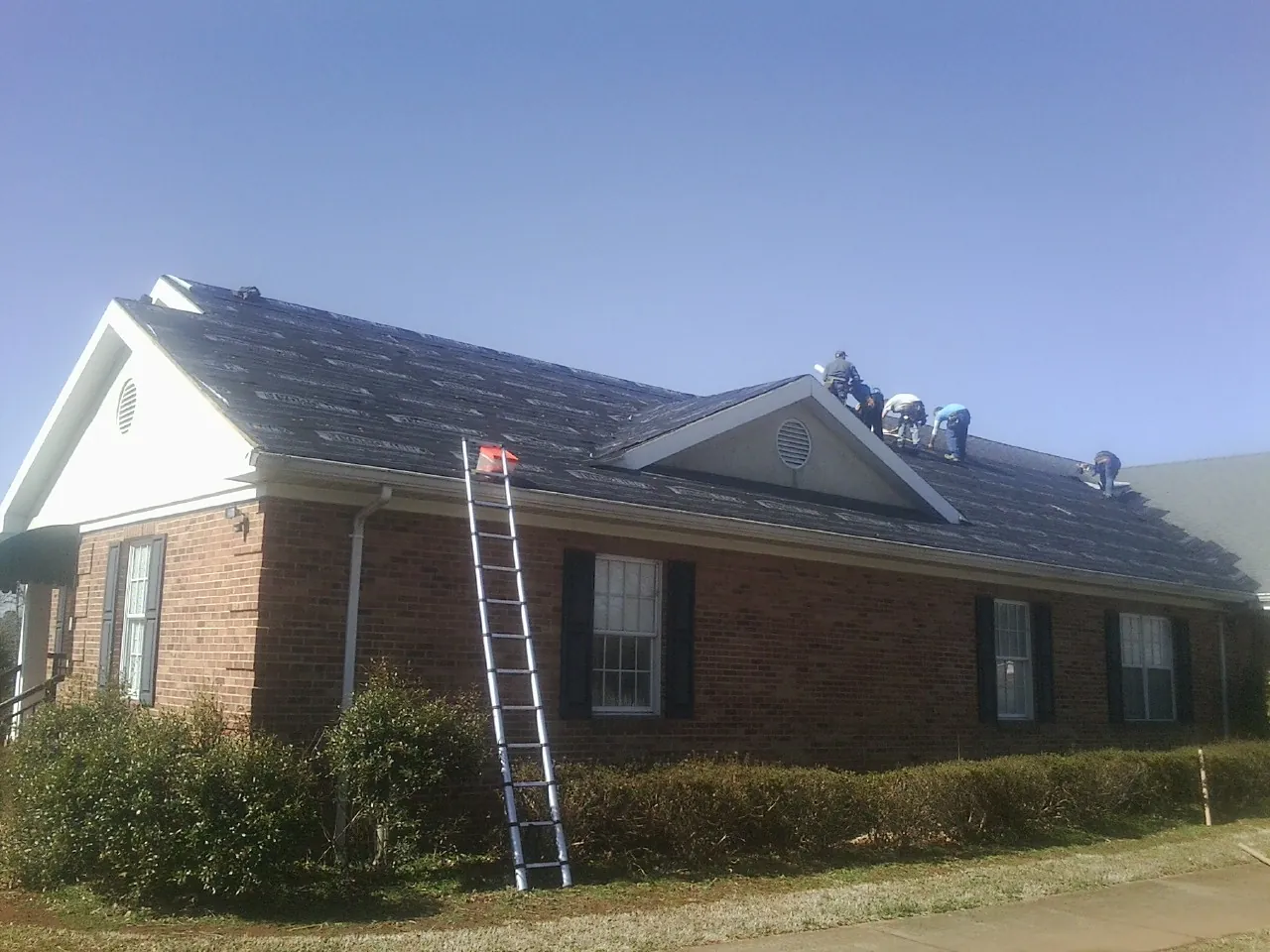 Crew tearing shingles off a brick ranch roof with a ladder set — Emergency Roof Repair work by our crew in Berrien Springs
