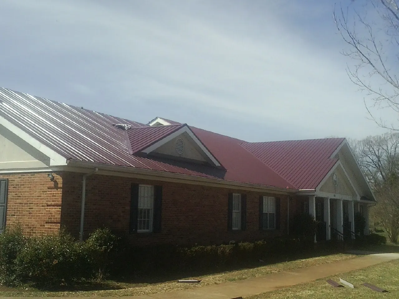 Red metal roof with gabled entries on a long brick building, from a Hail Damage Roof Repair job in Berrien Springs