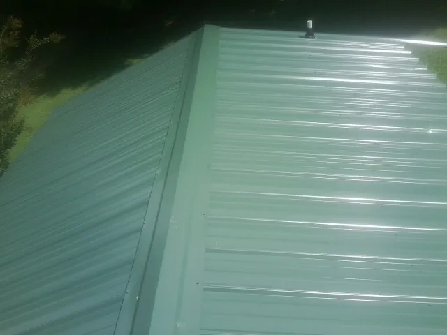 New green metal panels meeting at the ridge of a roof — Flat Roof Repair work by our crew in Berrien Springs