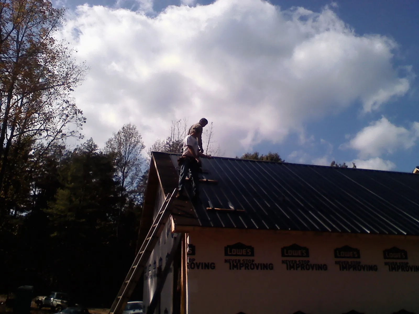 Roofer fastening dark metal panels high against a cloudy sky, from a Roof Inspection job in Berrien Springs