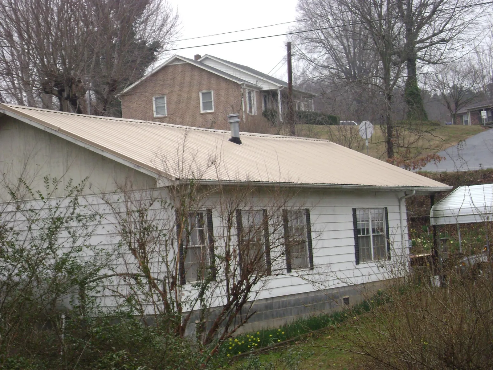 Tan metal roof on a white sided house set into a hillside — Commercial Roofing by Roofing Brothers in Berrien Springs