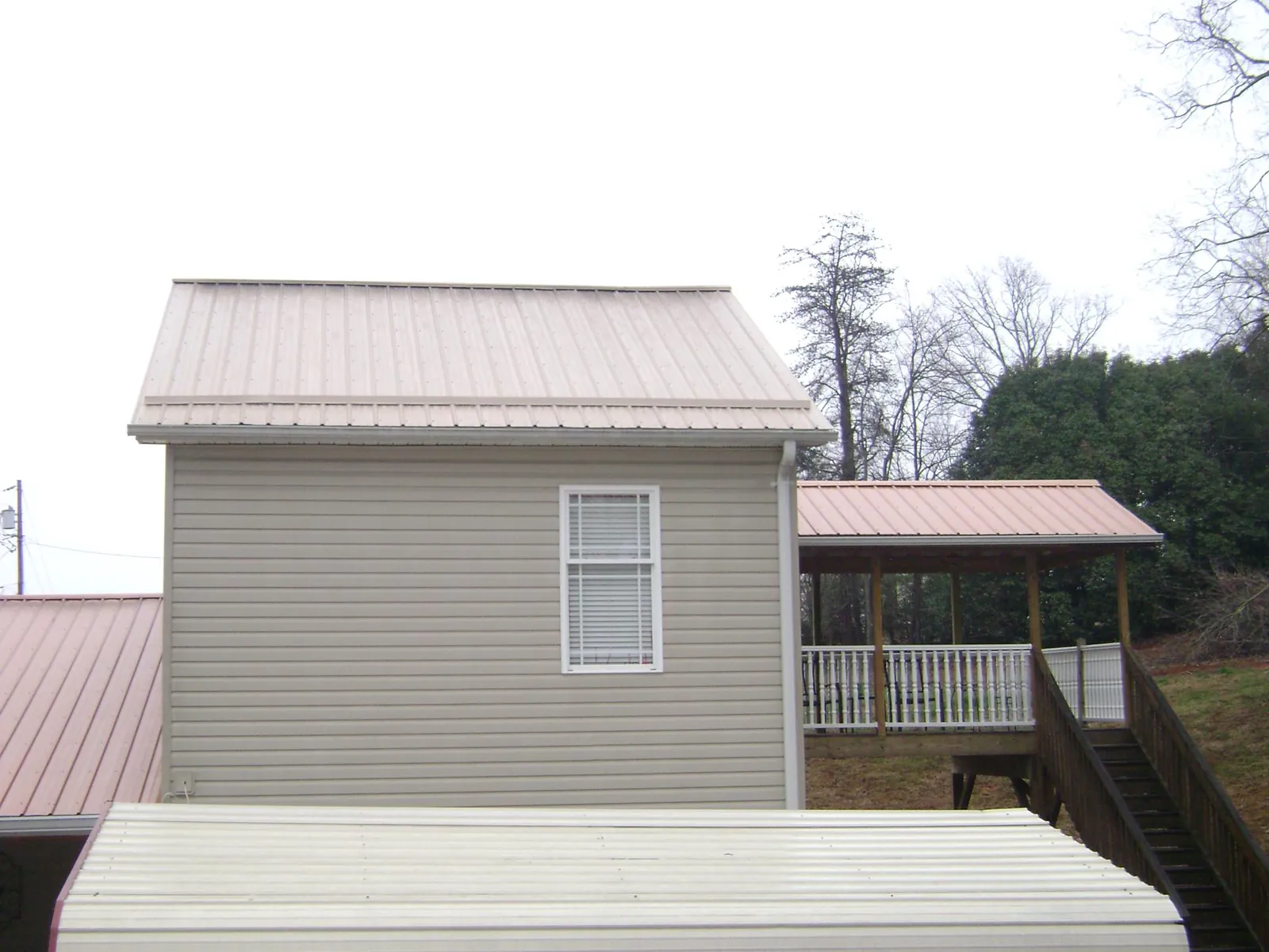Tan metal roofs on a two story addition and attached porch, from a Roof Replacement job in Berrien Springs
